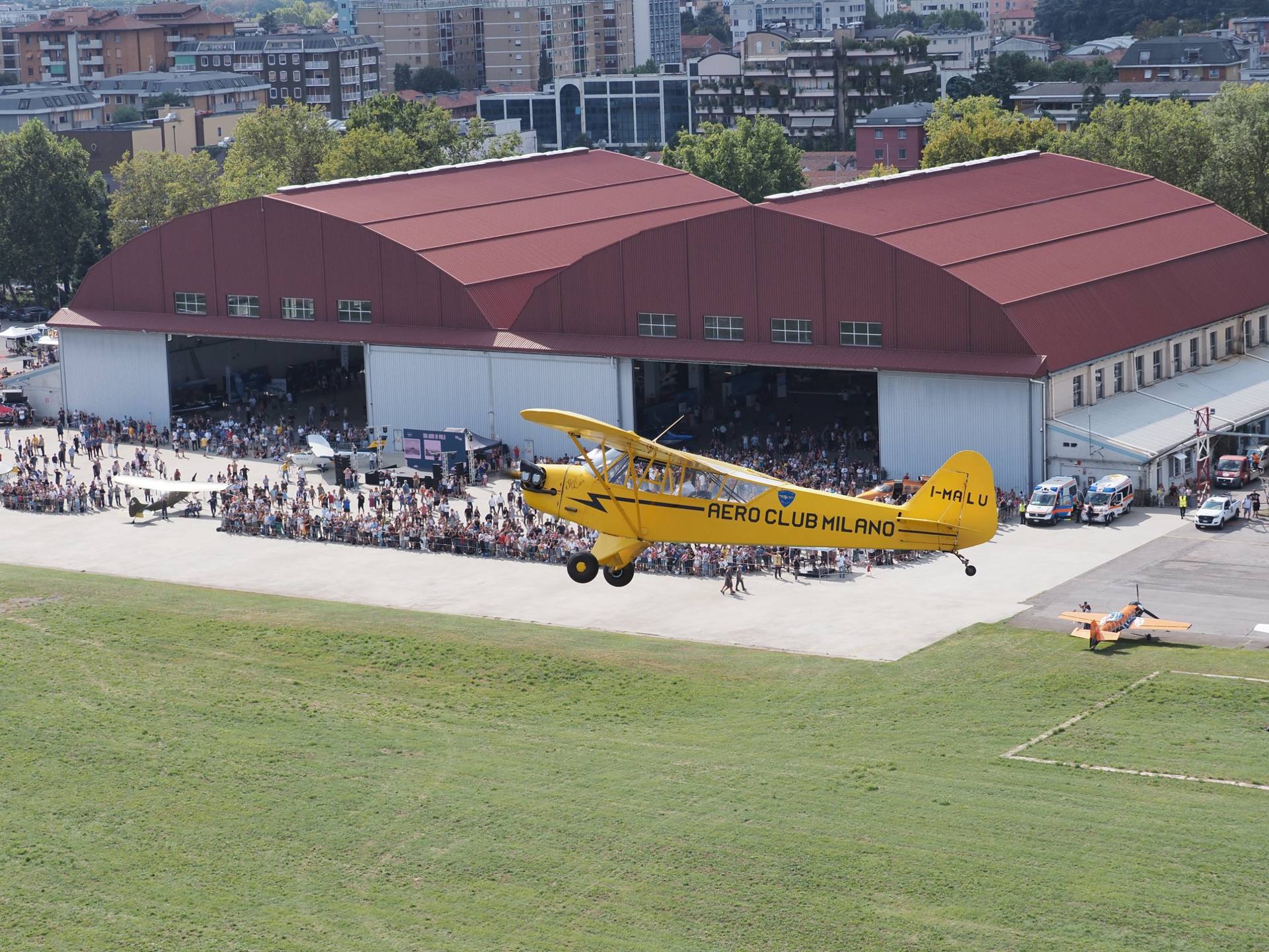 Il Piper I-MALU dell'Aero Club Milano sorvola la folla del Centenario davanti agli hangar dell'Aeroporto di Bresso